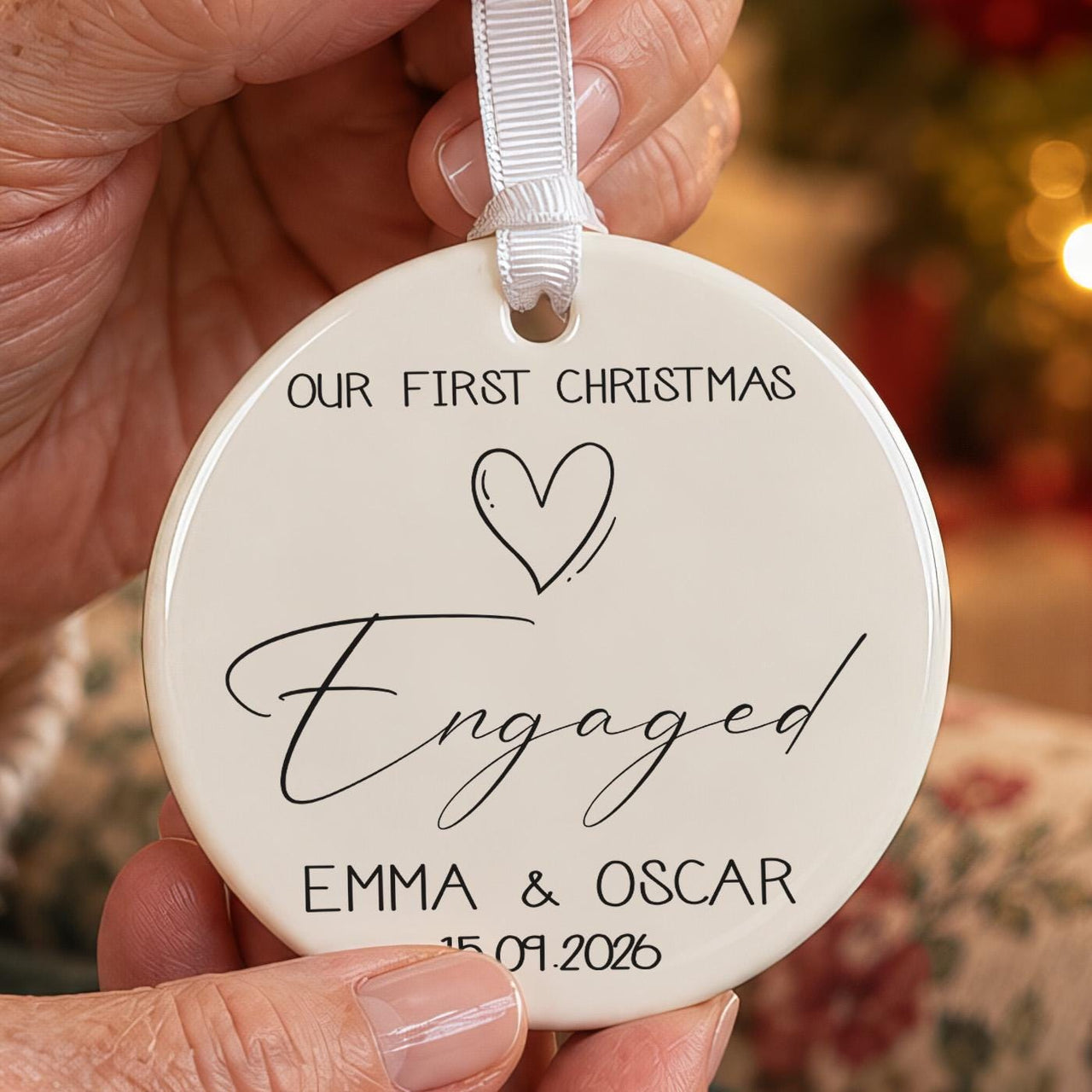 Round white ceramic bauble reading Our First Christmas Engaged with a heart, the names Emma and Oscar and a date