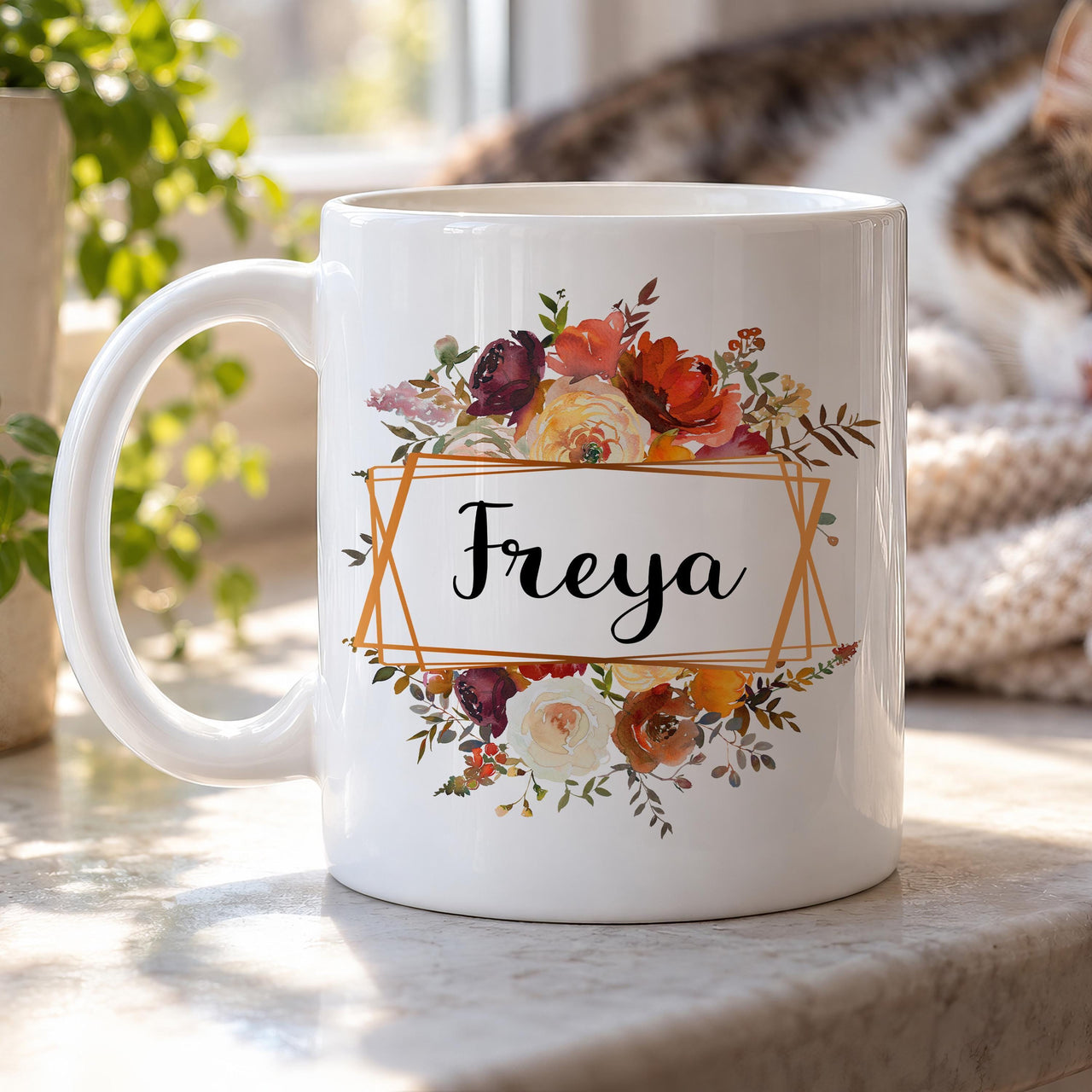 Personalised floral mug: white mug with autumn roses above and below a copper geometric frame holding Freya in script