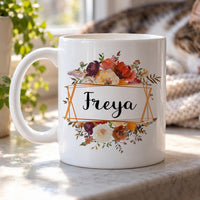 Personalised floral mug: white mug with autumn roses above and below a copper geometric frame holding Freya in script