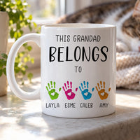 Personalised grandad mug: white mug with THIS GRANDAD BELONGS TO above four coloured handprints named LAYLA, ESME, CALEB, AMY