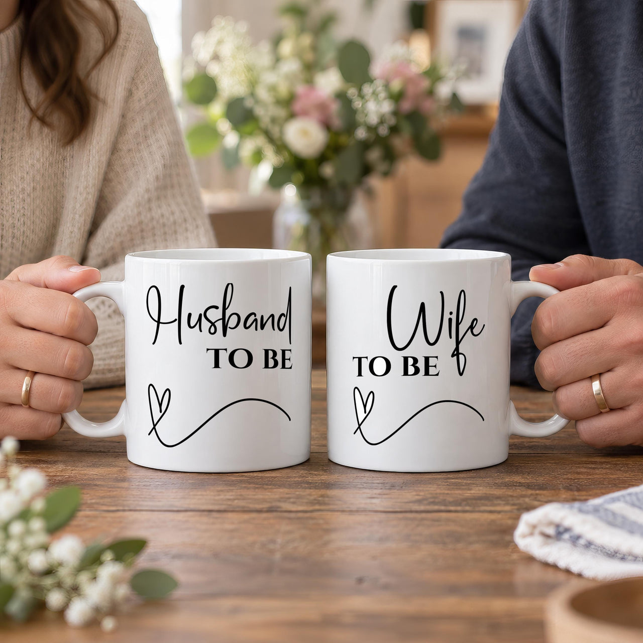 Engagement mug pair: two white mugs reading Husband TO BE and Wife TO BE in black script with a heart swirl