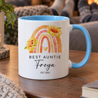 Personalised aunt mug: white mug with blue handle, a rainbow with sunflowers, BEST AUNTIE, the name Freya and EST. 2023