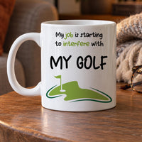 Funny golf mug: white mug reading My job is starting to interfere with MY GOLF above a green putting green and flag