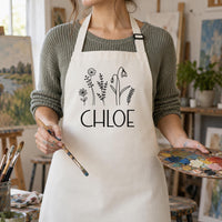 Natural cream apron with black wildflowers and 'CHLOE', worn in an art studio with a palette - personalised apron