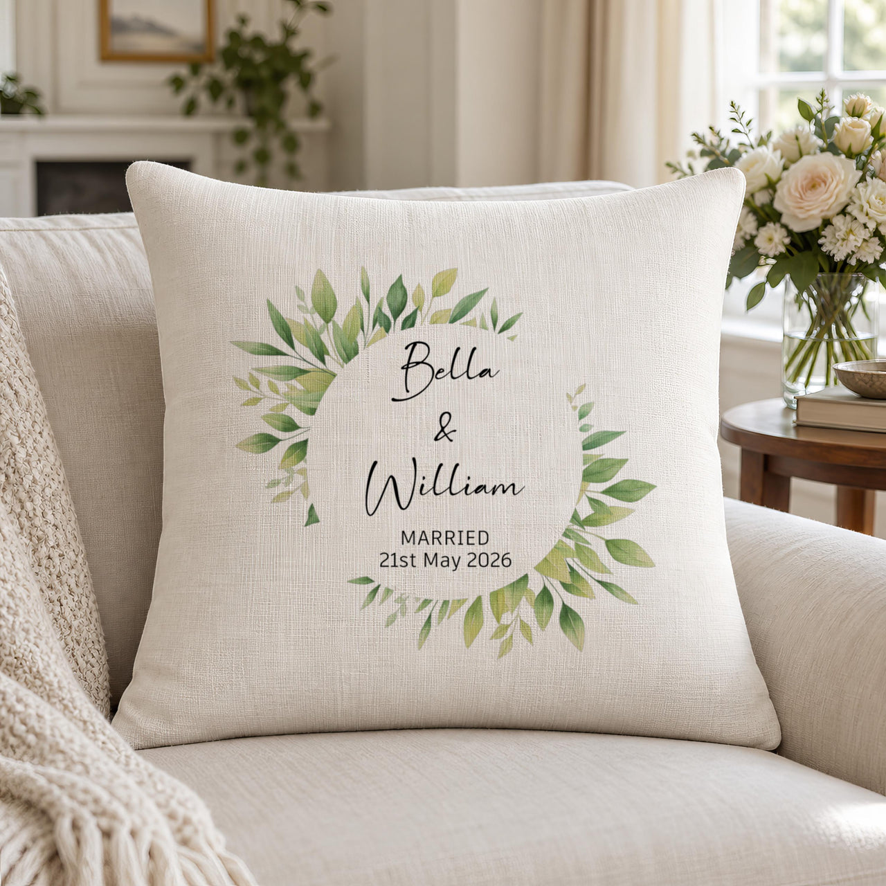 Linen-look cushion on a sofa with a green leaf wreath, 'Bella & William' and 'Married 21st May 2026' - personalised cushion
