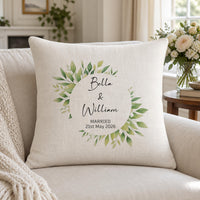 Linen-look cushion on a sofa with a green leaf wreath, 'Bella & William' and 'Married 21st May 2026' - personalised cushion