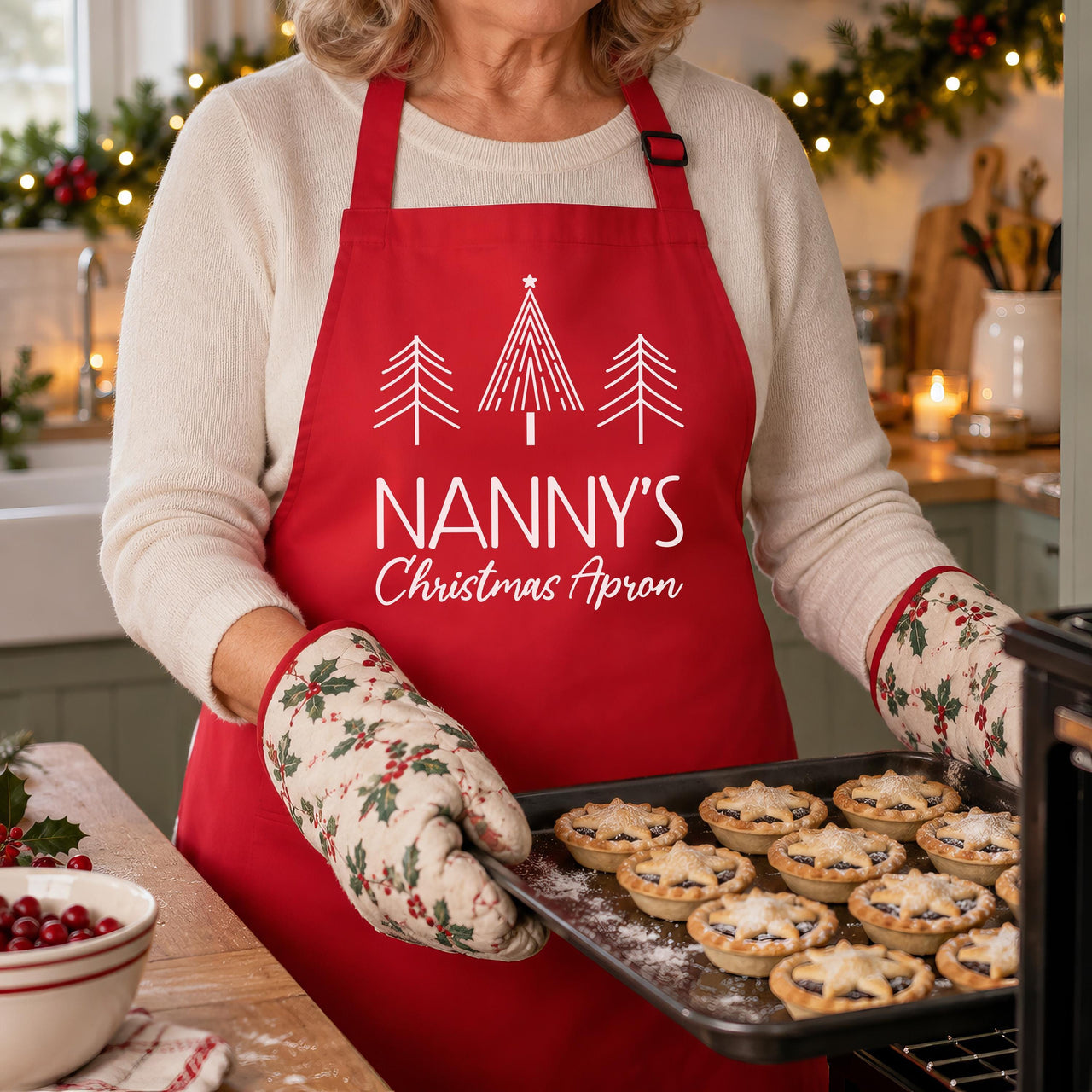Red Nanny's Christmas Apron with three line-art trees, worn while taking biscuits out of the oven