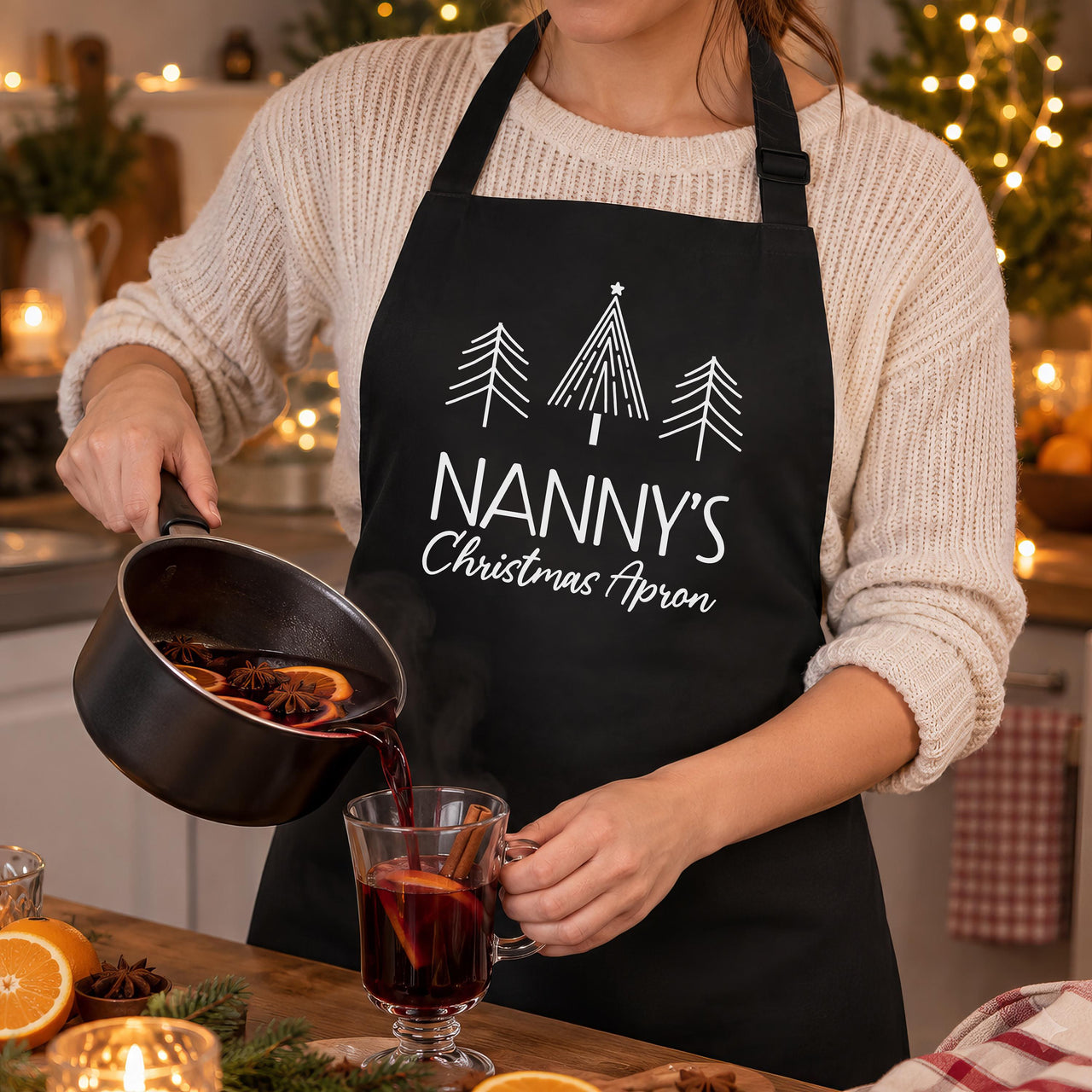 Black Nanny's Christmas Apron with white tree print, worn while pouring mulled wine