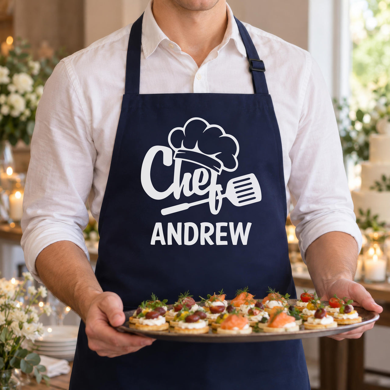 Navy apron with white "Chef" and "ANDREW" print, worn while serving a tray of canapes at a party - personalised apron