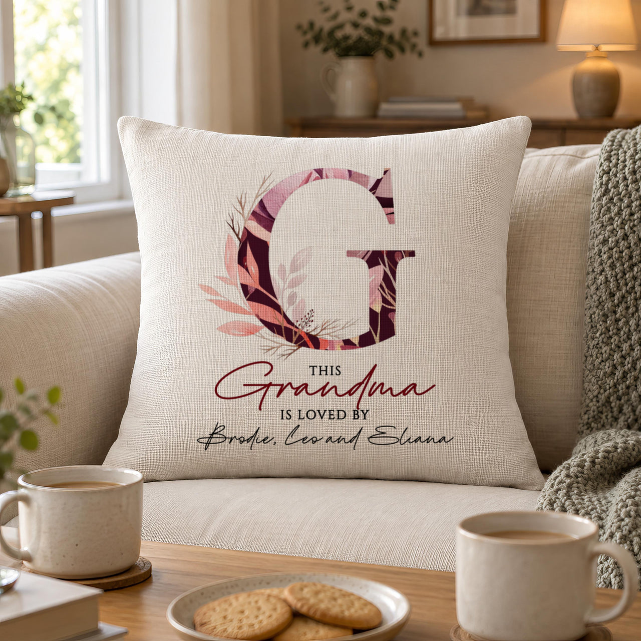 Linen-look floral letter G 'Grandma' cushion on a sofa with mugs and biscuits - personalised cushion