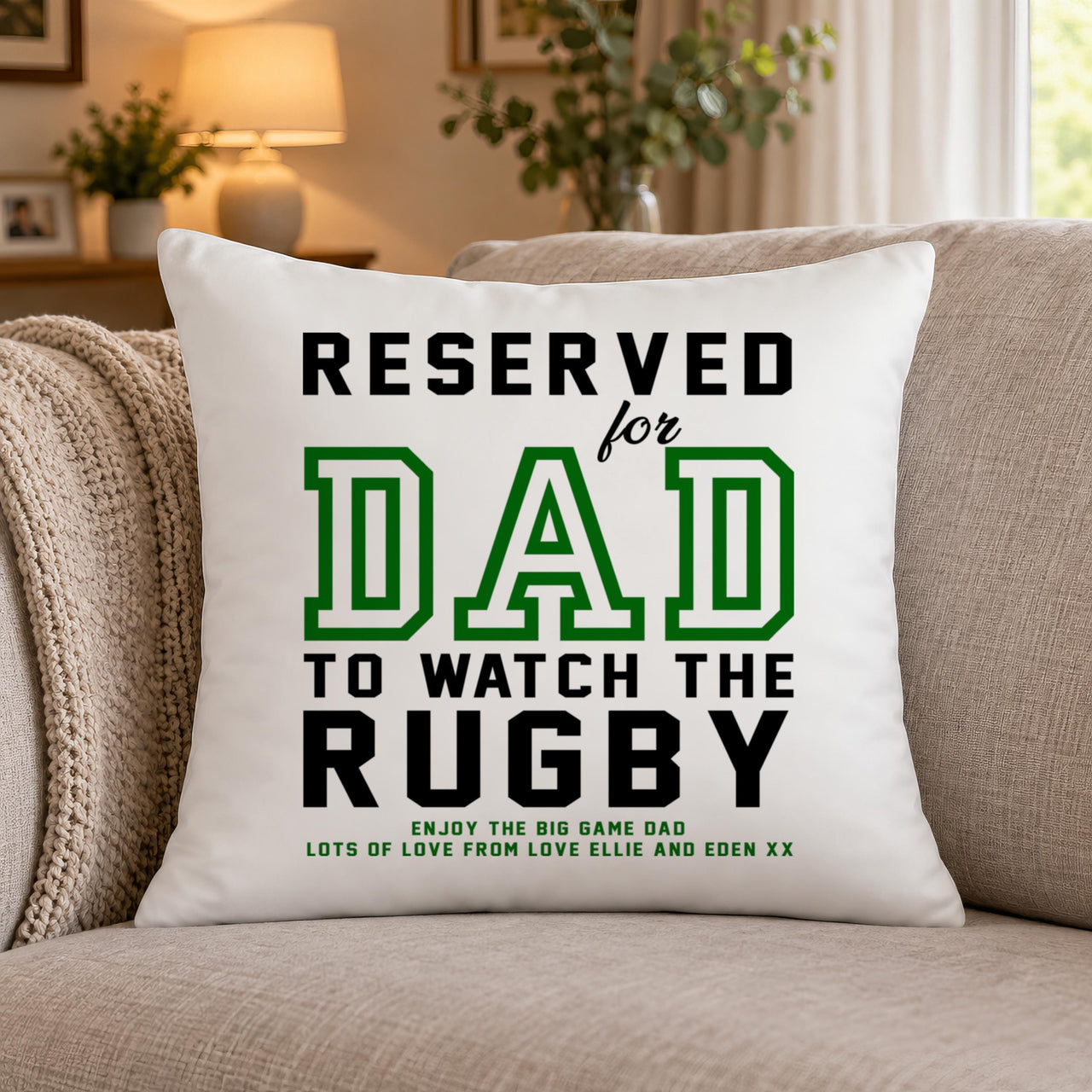 White cushion with green and black 'RESERVED for DAD TO WATCH THE RUGBY' text on a sofa - personalised cushion