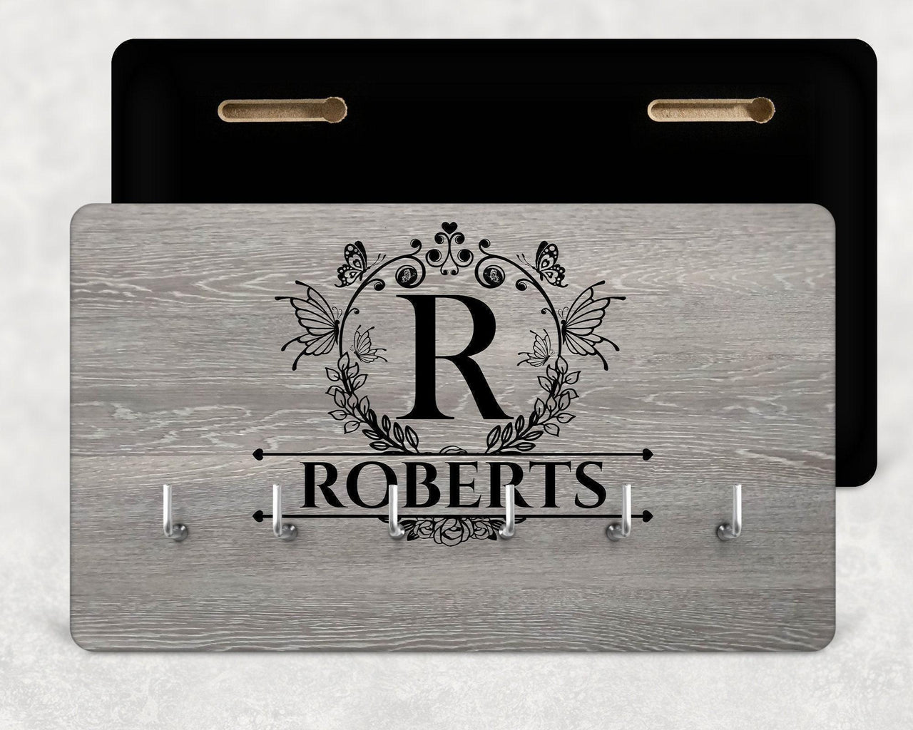Grey wood-effect board, butterfly wreath 'R' monogram, 'ROBERTS' and six hooks, black back shown - personalised key holder