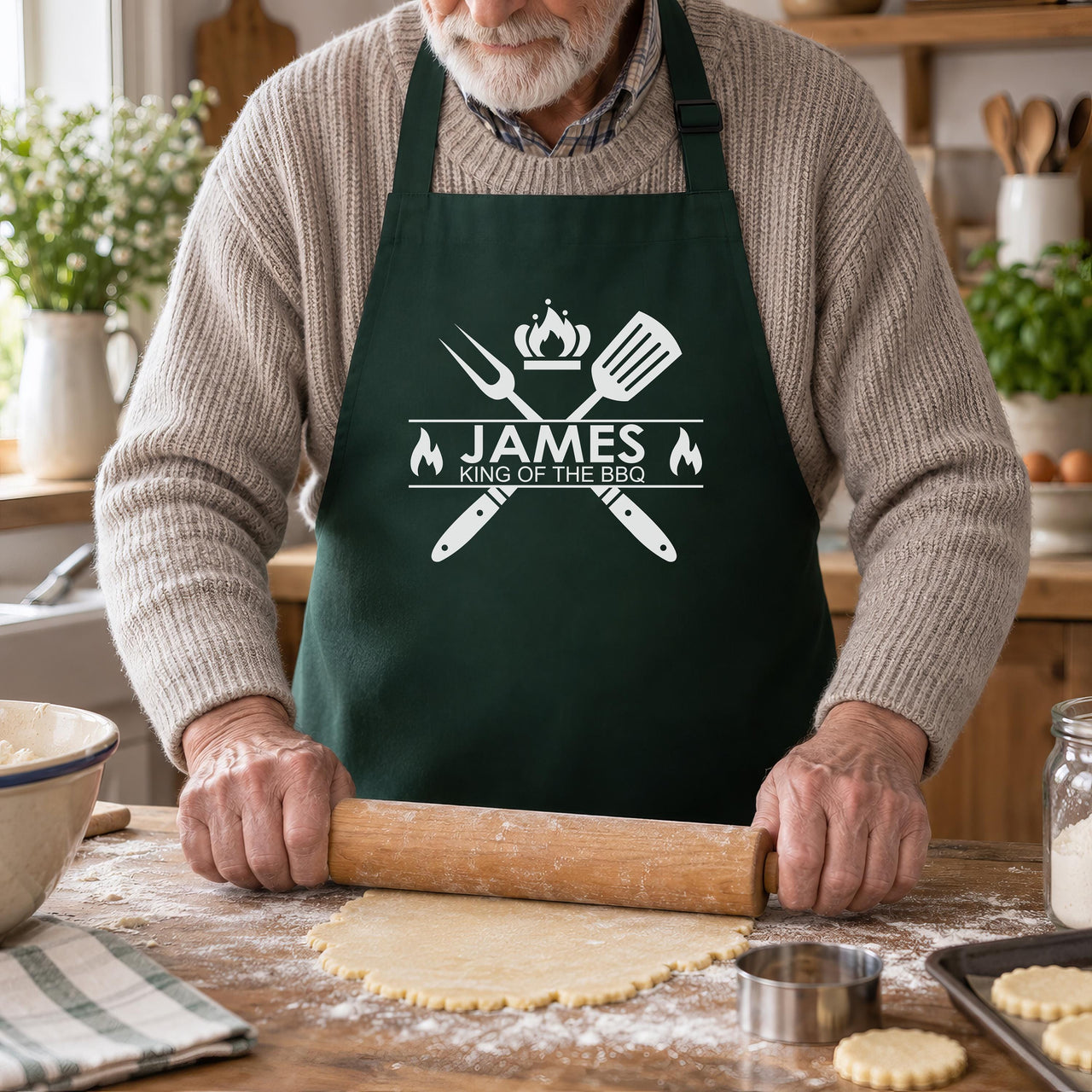 Older man rolling pastry in a bottle green apron printed "JAMES King of the BBQ" in white - personalised apron