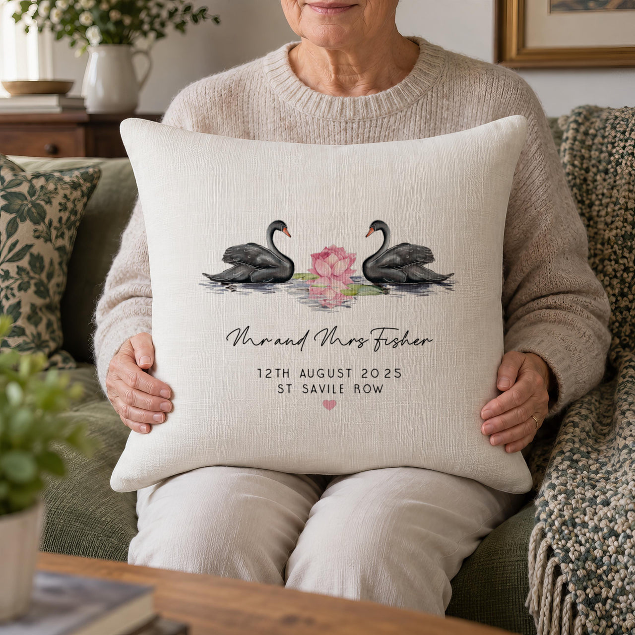 Woman holding a cream cushion showing two black swans, 'Mr and Mrs Fisher' and '12th August 2025' - personalised cushion