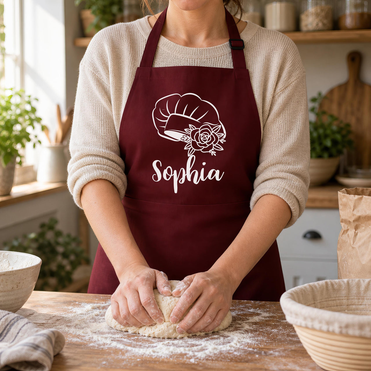 Burgundy apron with a white chef hat and rose outline above "Sophia", worn while kneading dough - personalised apron