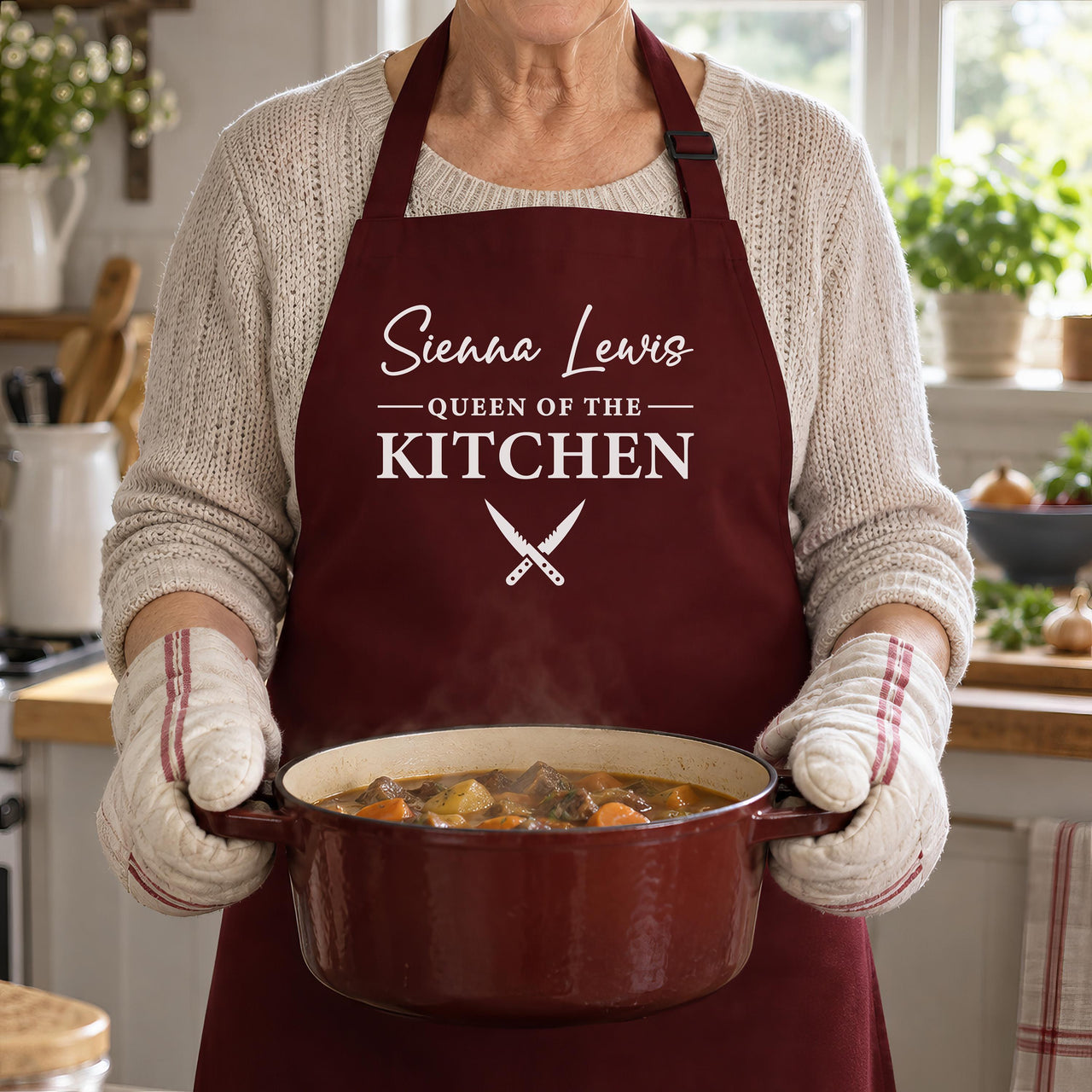 Burgundy Queen of the Kitchen apron with a name, worn while carrying a casserole pot
