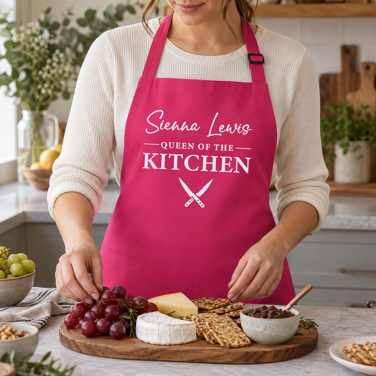 Pink Queen of the Kitchen apron with a name, worn while laying out a cheese board