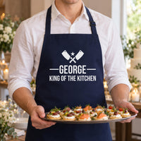 Man serving canapes at a party in a navy apron printed 'GEORGE King of the Kitchen' - personalised apron