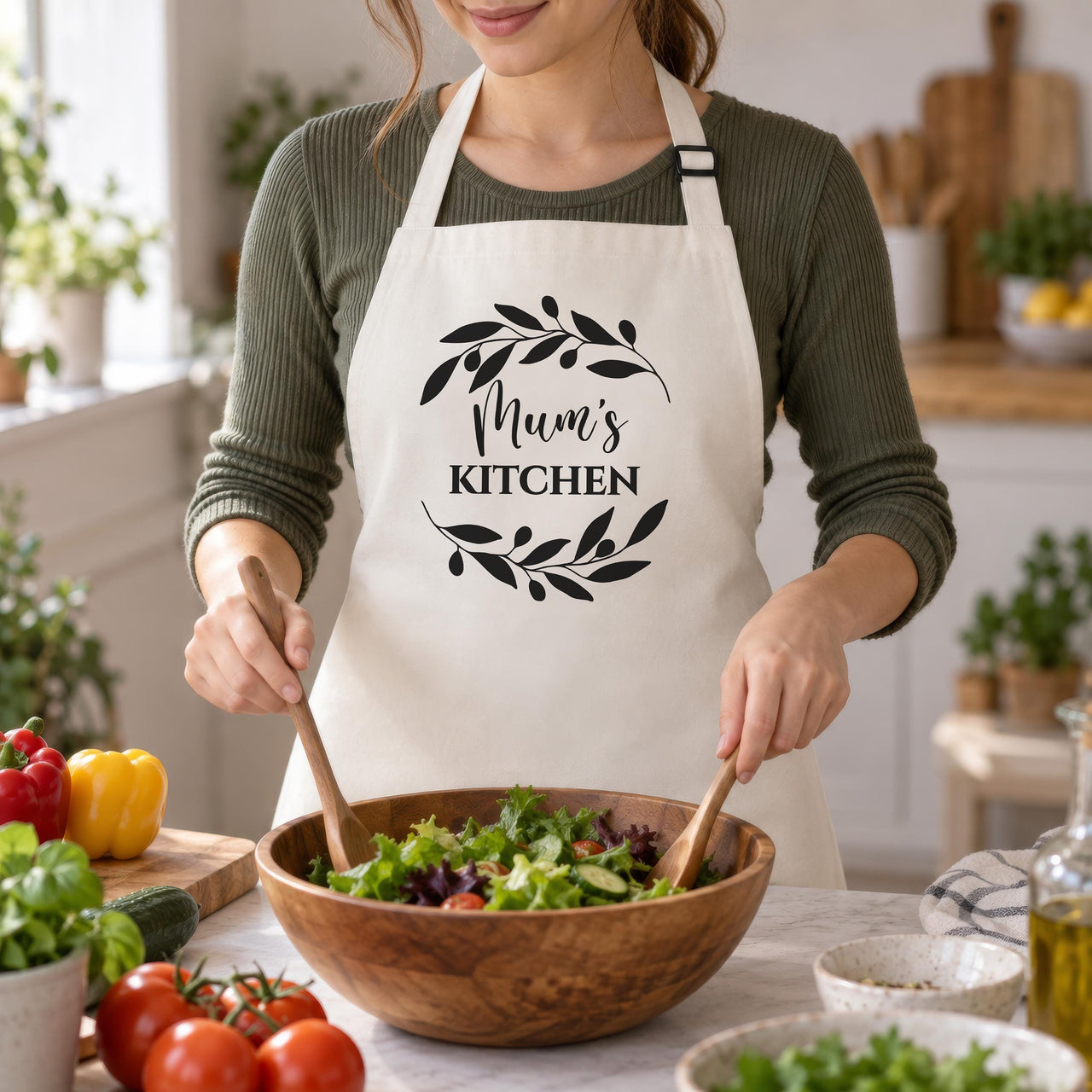 White Mum's Kitchen apron with a black leaf wreath, worn while tossing a salad