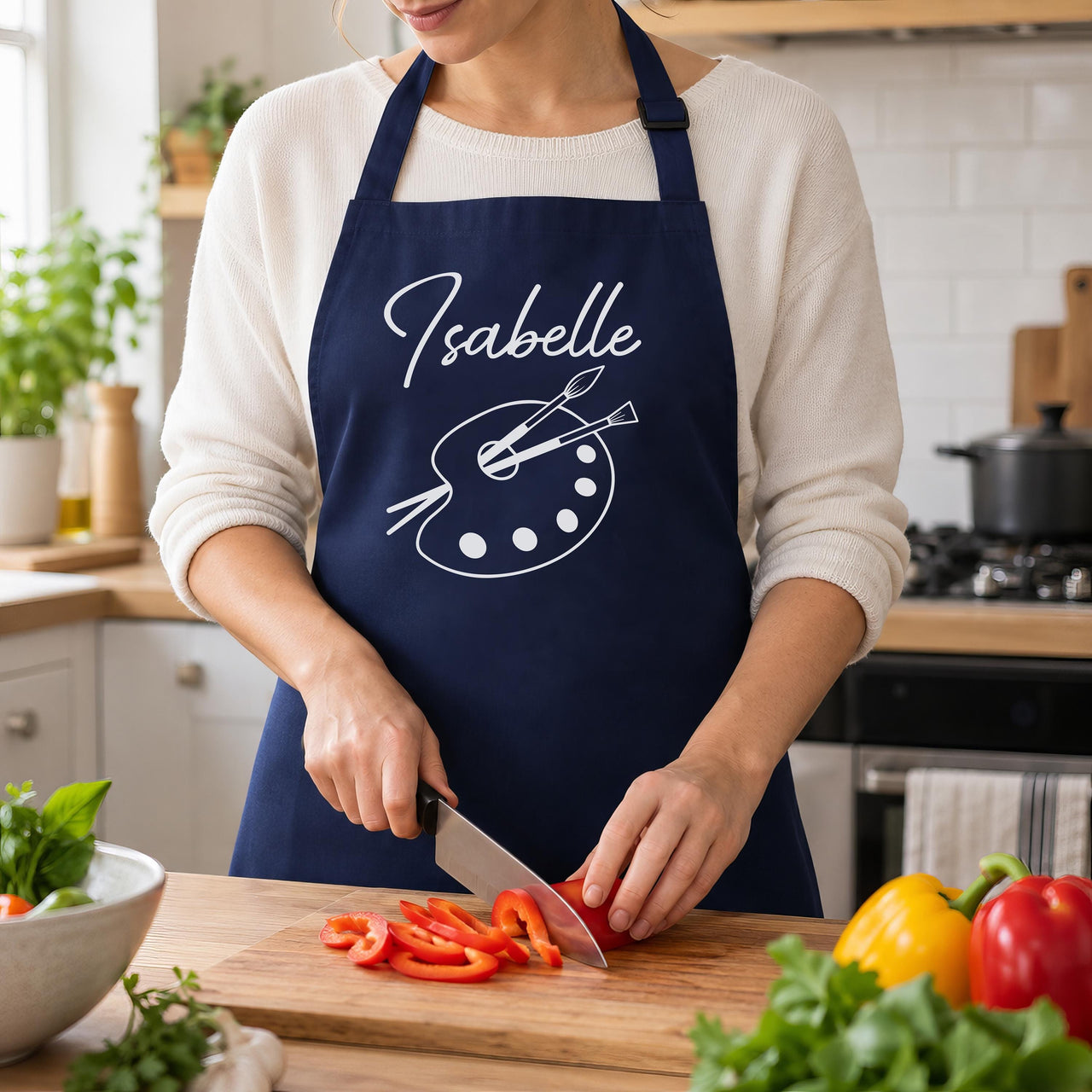 Navy apron with white 'Isabelle' and paint palette, worn while slicing peppers - personalised apron