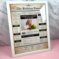 White framed birthday newspaper poster for a 40th with a woman holding tulips, on a pink and marble surface