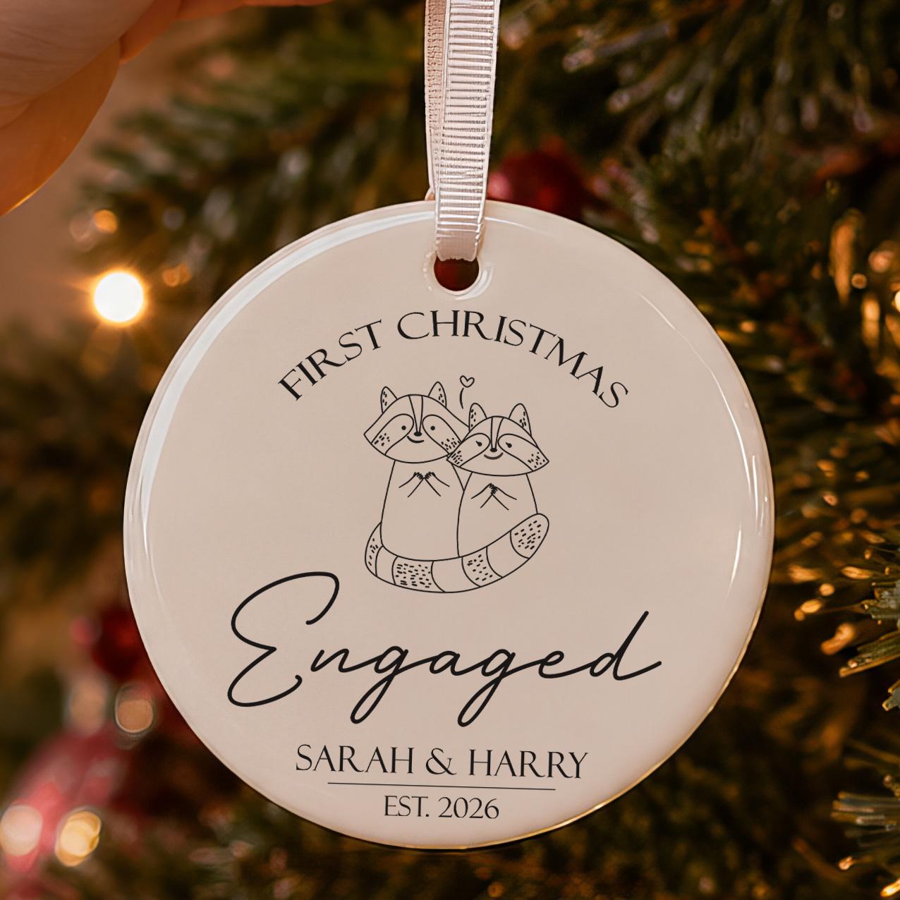 First Christmas engaged bauble: ceramic ornament with two line-art raccoons hugging and Sarah & Harry Est. 2026