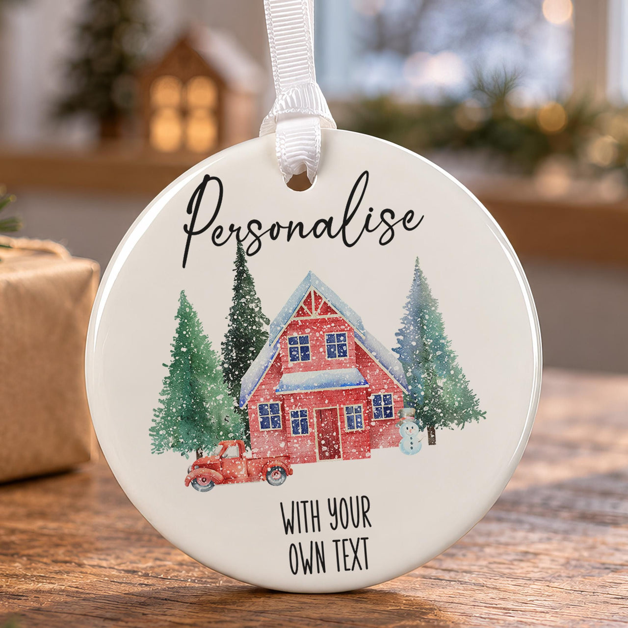 Round white ceramic bauble with a red cottage, snowy fir trees and a red truck, with sample text above and below