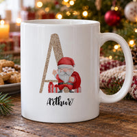 Personalised Christmas initial mug: white mug with a gold glitter letter A, a cartoon Santa with presents and Arthur