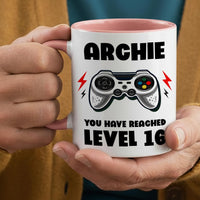 Personalised gamer mug: white mug with pink handle, the name ARCHIE, a game controller and YOU HAVE REACHED LEVEL 16