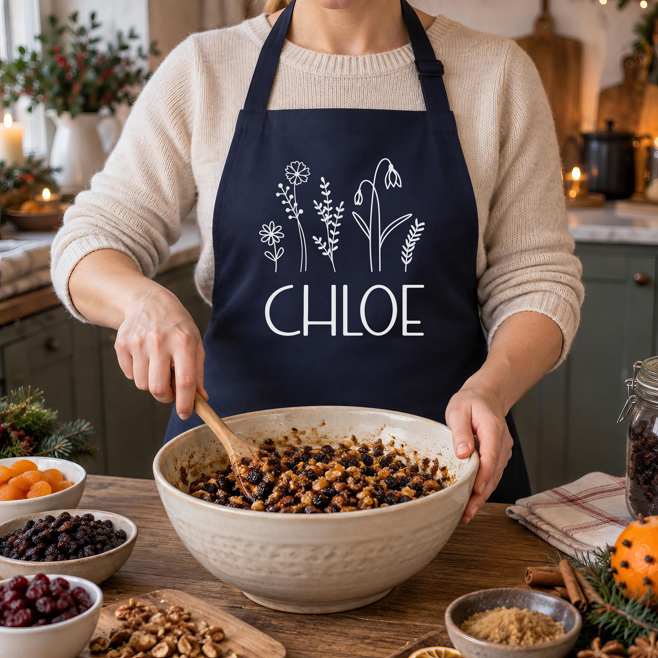 Navy apron with white wildflowers and 'CHLOE', mixing Christmas pudding fruit in a bowl - personalised apron