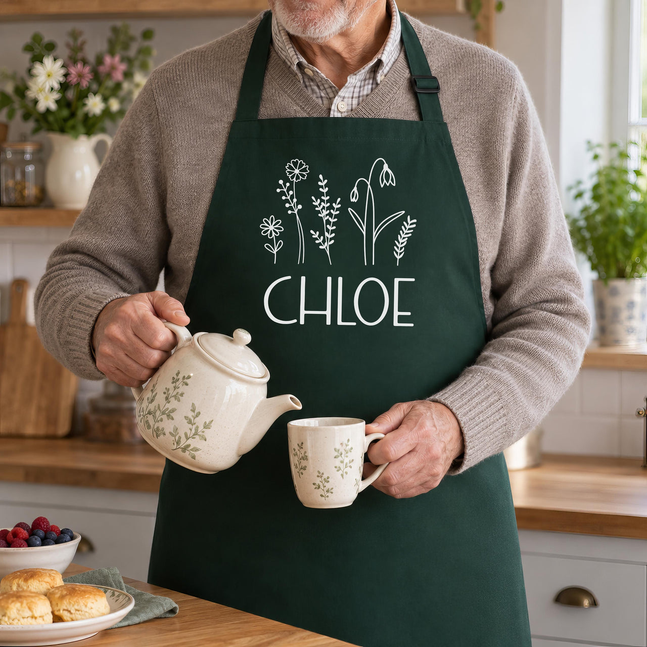 Bottle green apron with white wildflowers and 'CHLOE', worn by a man pouring tea - personalised apron
