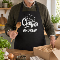 Man in a black apron with white chef hat, spatula and 