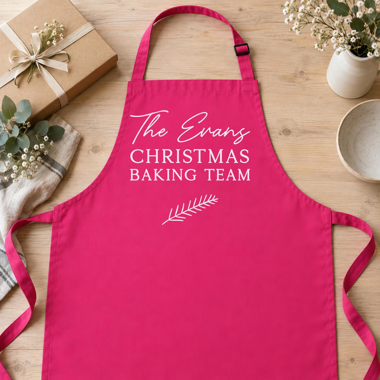 Pink apron reading 'The Evans CHRISTMAS BAKING TEAM' laid flat with a gift box - personalised apron