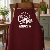 Burgundy apron with white chef hat and spatula print and the name 
