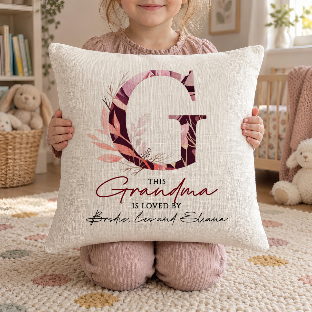 Child holding a linen-look cushion with floral letter G and 'THIS Grandma IS LOVED BY' - personalised cushion