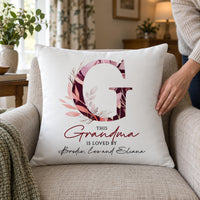White cushion with pink floral letter G and 'THIS Grandma IS LOVED BY' names on an armchair - personalised cushion