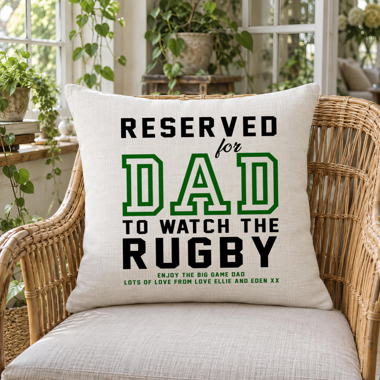Linen-look cushion reading 'RESERVED for DAD TO WATCH THE RUGBY' on a wicker chair - personalised cushion