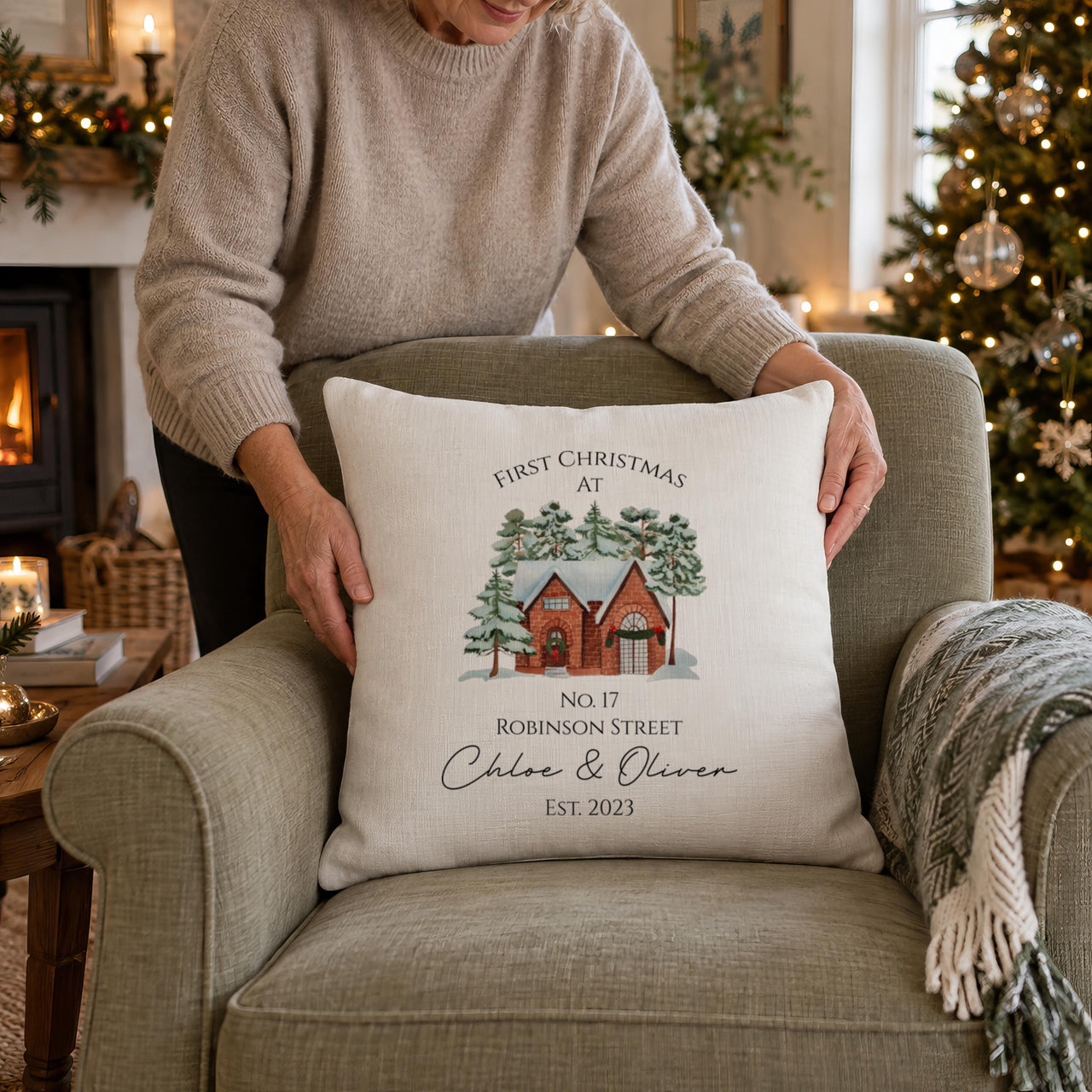 Linen-look new home Christmas cushion 'Chloe & Oliver Est. 2023' placed on a green armchair by a tree - personalised cushion