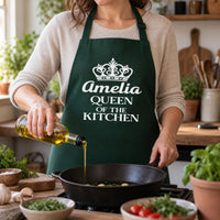 Bottle green apron with crown and 'Amelia QUEEN OF THE KITCHEN' pouring oil into a pan - personalised apron