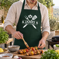 Man brushing sauce on kebabs in a dark green apron with 