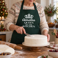 Bottle green apron with crown and 'Amelia QUEEN OF THE KITCHEN', icing a Christmas cake - personalised apron