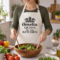 Natural cream apron with black crown and 'Amelia QUEEN OF THE KITCHEN', tossing a salad - personalised apron