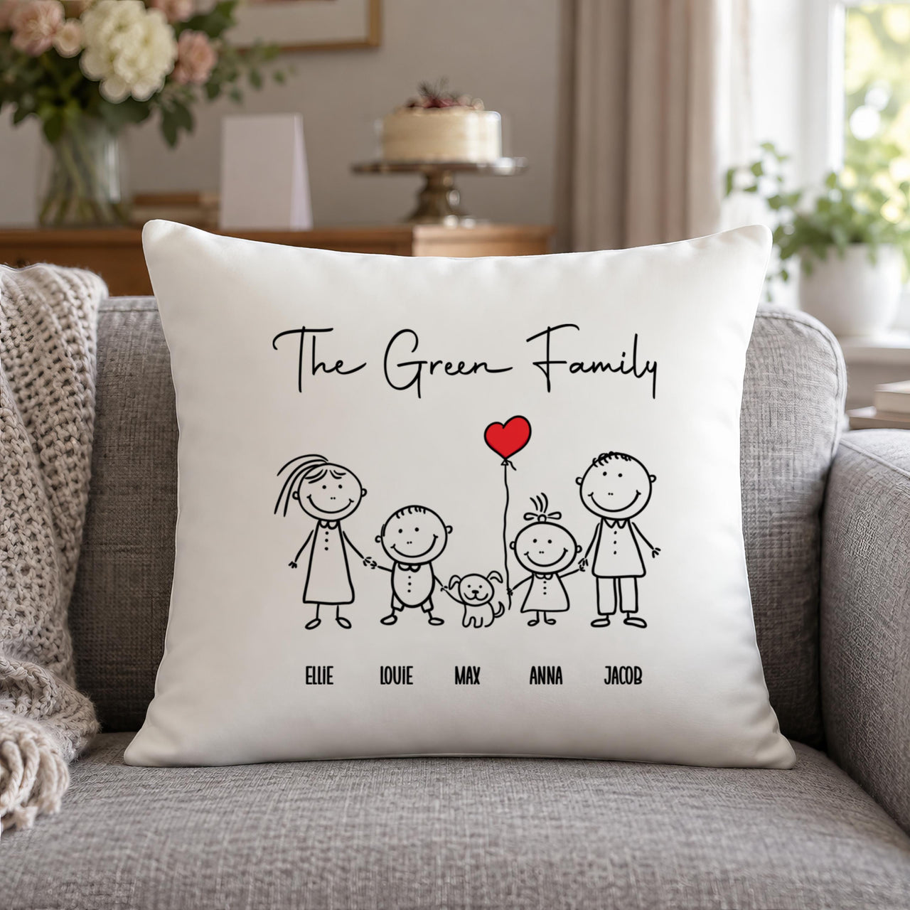 White 'The Green Family' stick figure cushion with 'ELLIE', 'LOUIE', 'MAX', 'ANNA', 'JACOB' on a sofa - personalised cushion
