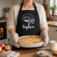 Woman in a black apron with white chef hat, rose and the name 