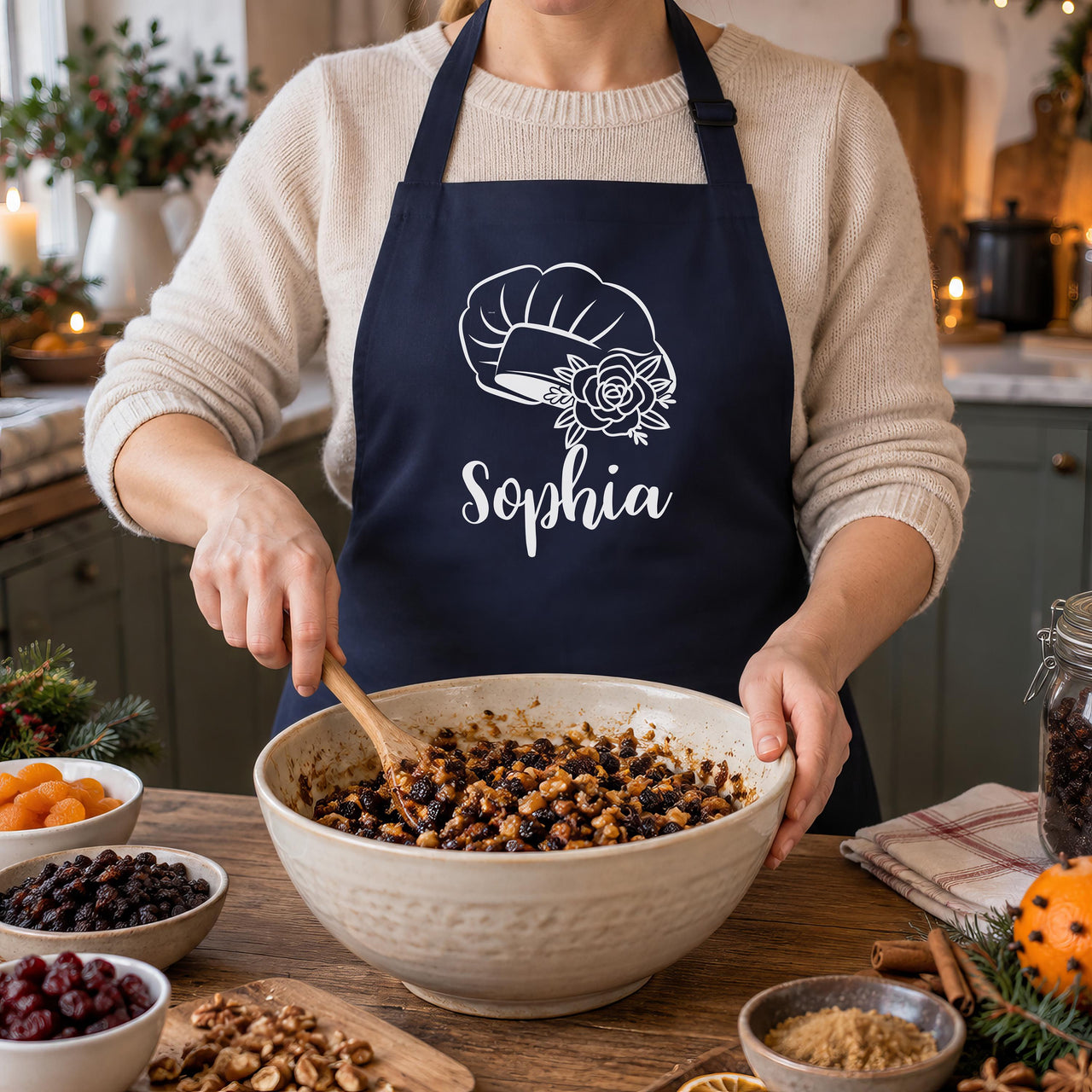 Navy apron with white chef hat, rose and "Sophia" worn while mixing Christmas cake fruit in a bowl - personalised apron