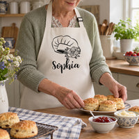 Older woman in a cream apron with black chef hat, rose and 