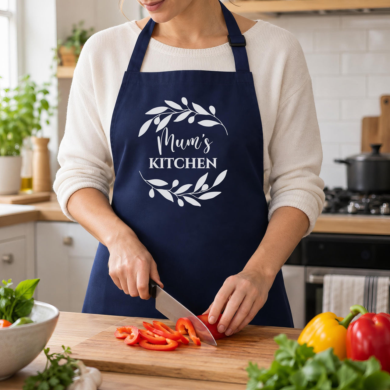 Navy Mum's Kitchen apron with a leaf wreath, worn while chopping red peppers