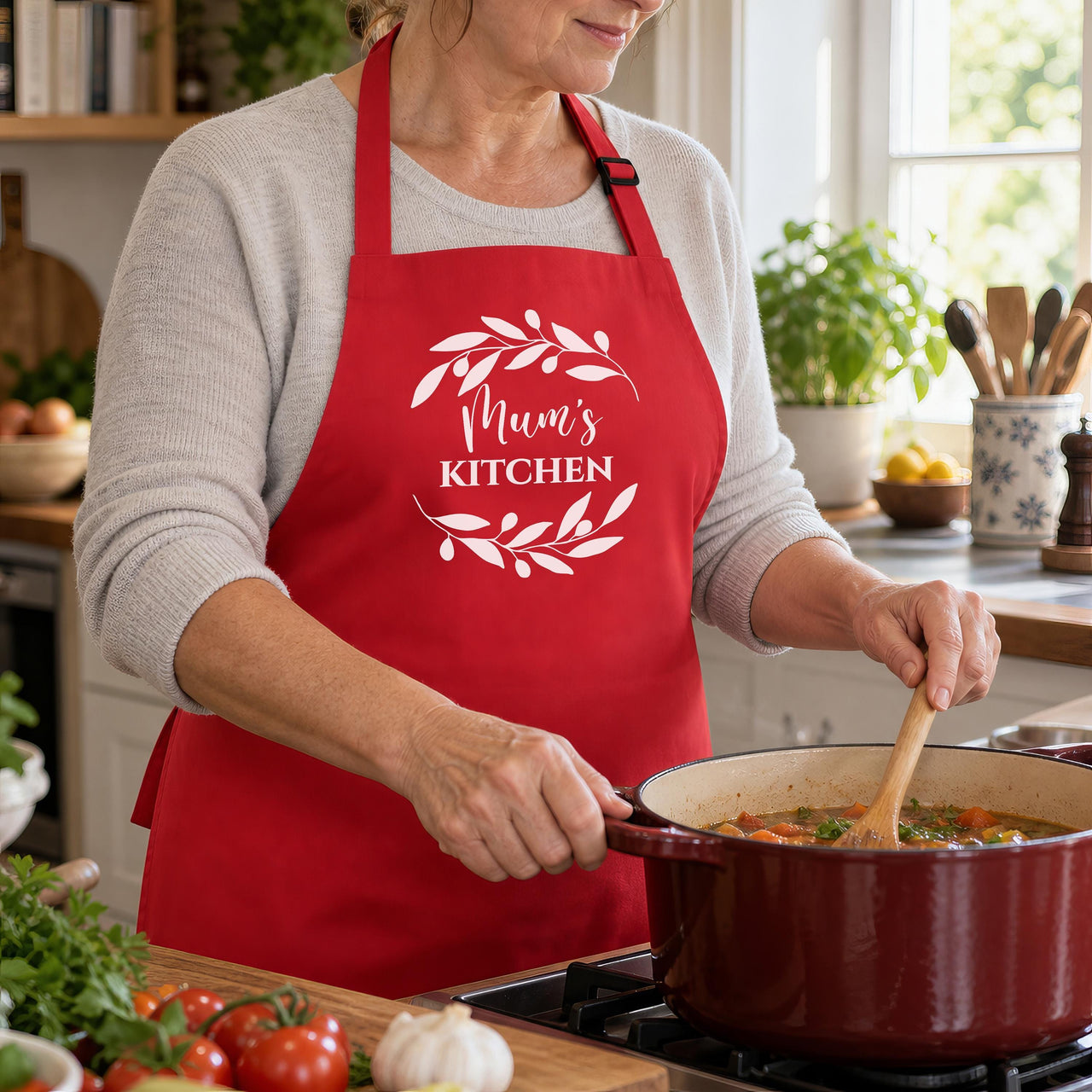 Red Mum's Kitchen apron with a leaf wreath, worn while stirring a pot on the hob