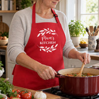 Red Mum's Kitchen apron with a leaf wreath, worn while stirring a pot on the hob