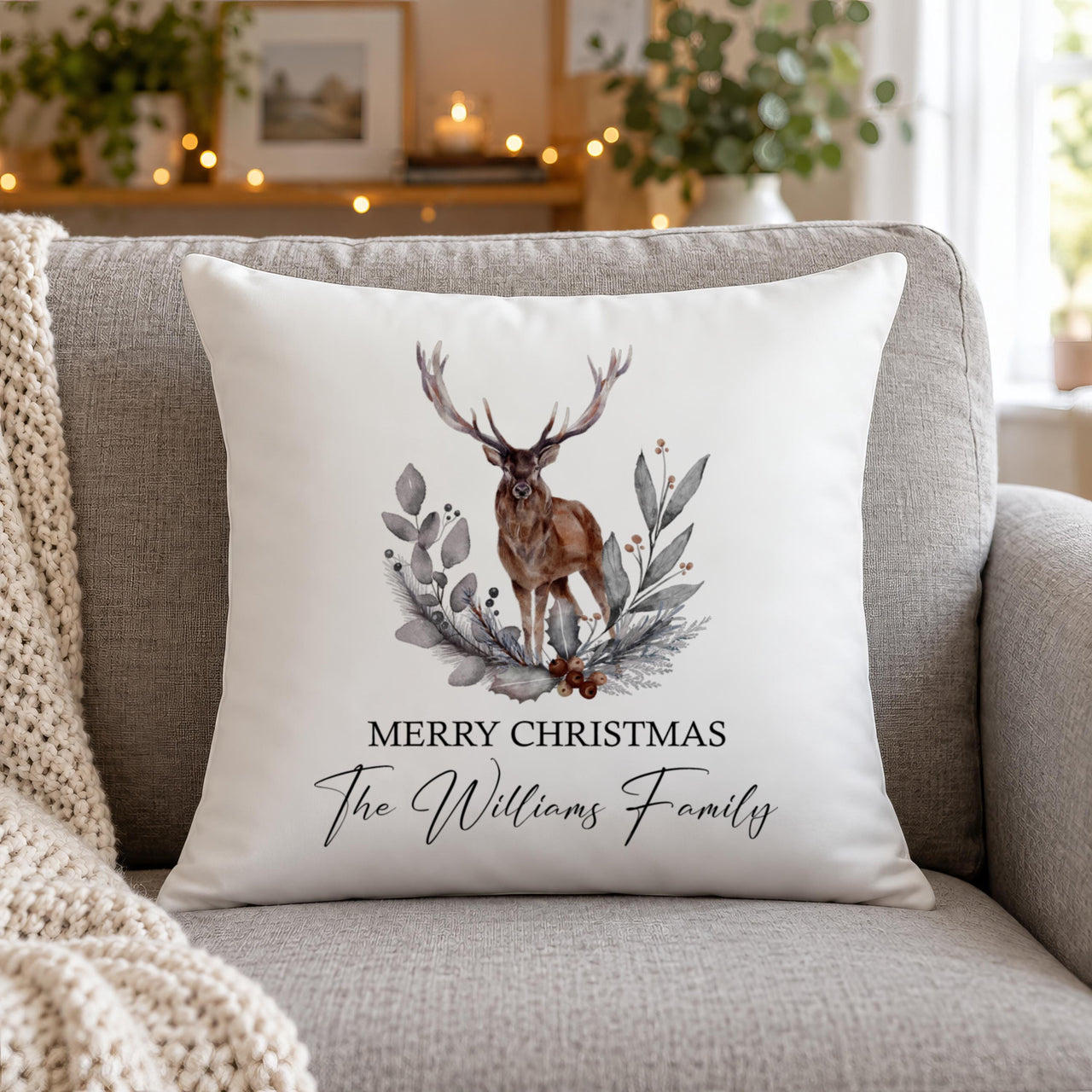 White cushion on a grey sofa, stag and foliage wreath, "Merry Christmas The Williams Family" - personalised cushion cover